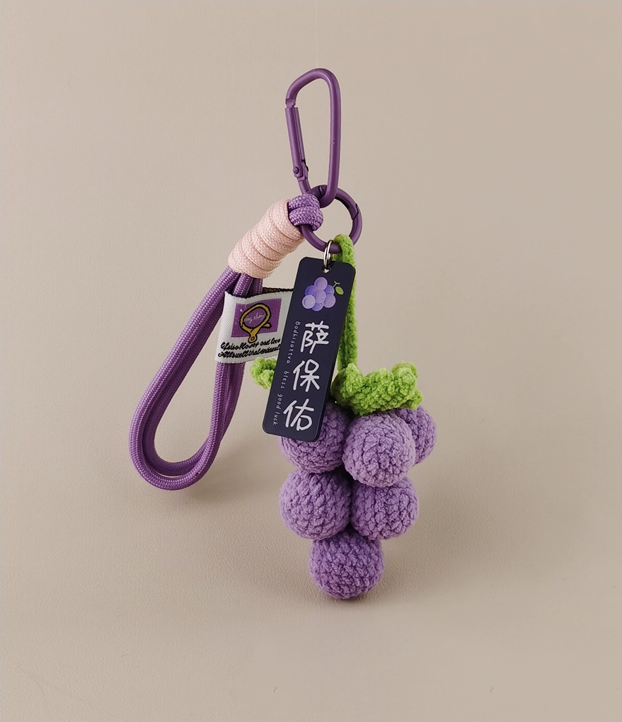 Wine grape keychain, purple with green highlights, crocheted style, tag hanging on the vine with the text "Uva Huilen" (a made-up word), product photography, simple background, high resolution, highly detailed.
