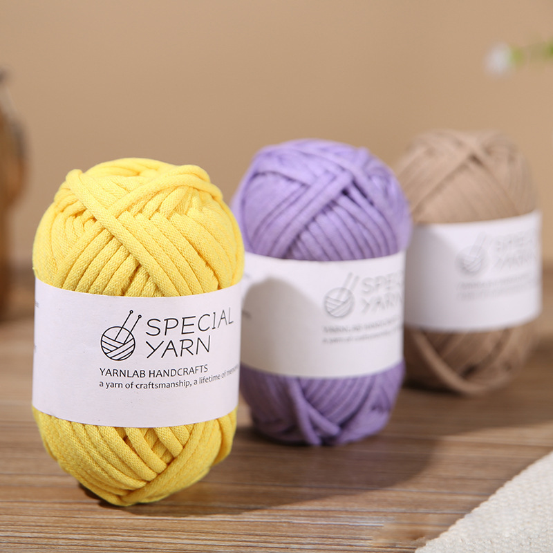 Three balls of soft, smooth, solid-colored, thick cotton thread in light yellow, beige, and purple colors, with a white label featuring the text "Sensational Special Handcrafts" in the middle, on a table background, product photography.