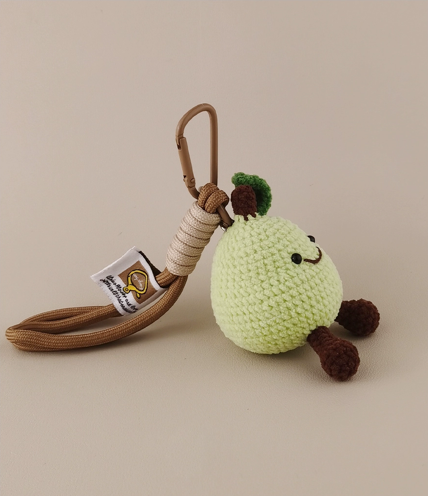 Cute green pear amigurumi keychain, with a tag and carabiner on the back, photographed from an angle against a beige background in high resolution.