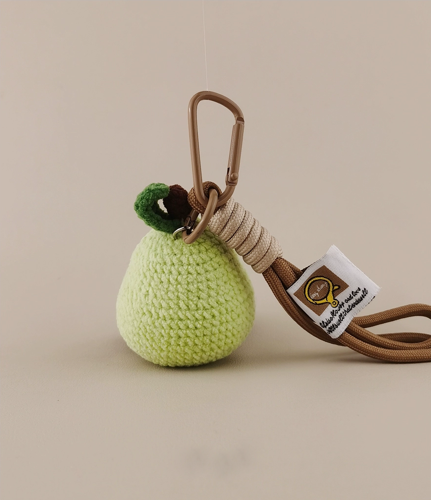 A cute little green pear, with knitted texture and crochet style, is hanging on the car seat". A small brown parac Closed lanyard attached to it "with white label", on solid color background. Product photography, real shot, high definition. The light source from top left corner of screen, professional product design images.