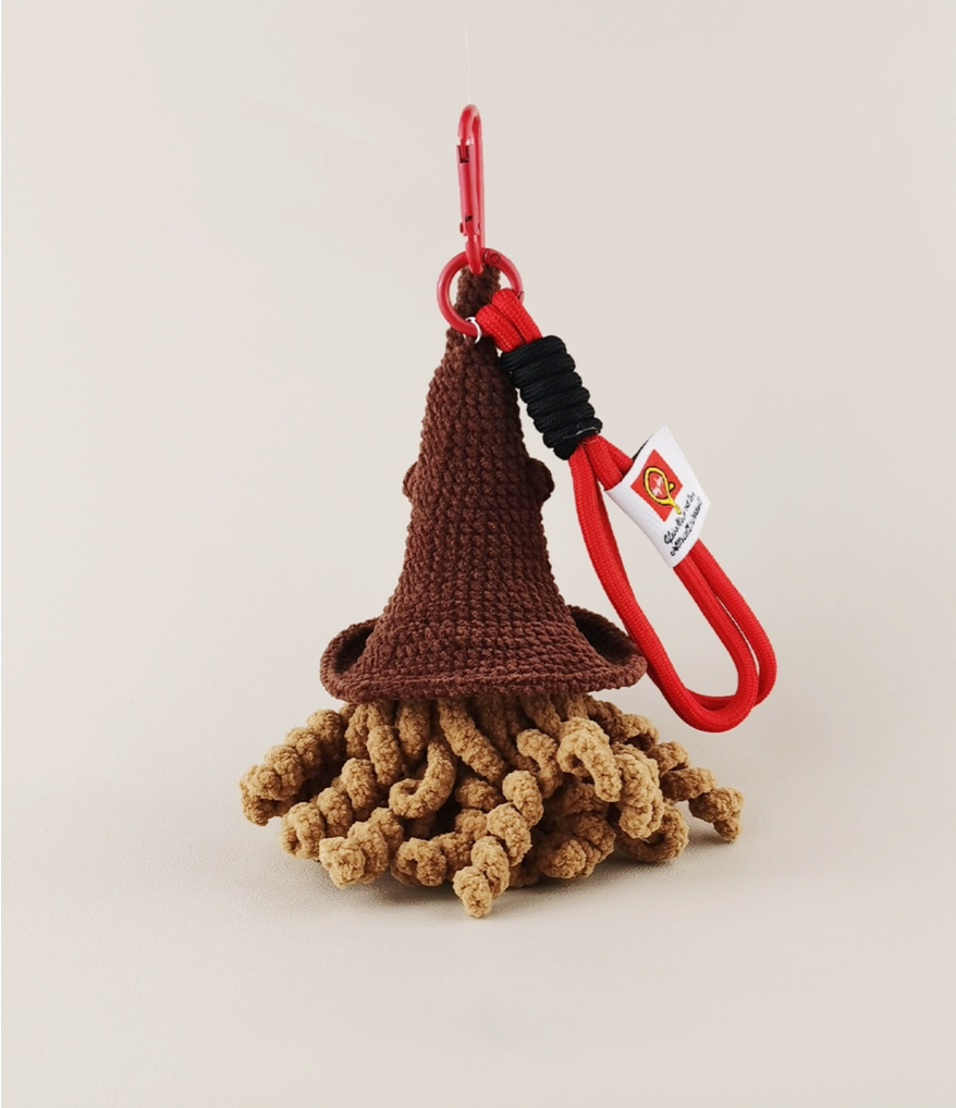  A knitted broom-handle hat made of brown yarn with a red, car-inspired, biomechanical design. The hat has a red plastic keychain hanger and a tag attached to it, all set against a white background