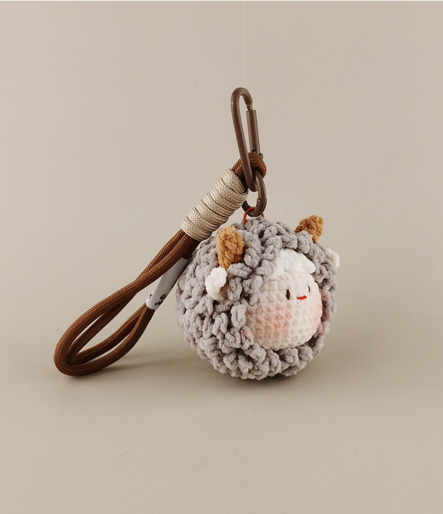Cute little sheep amigurumi pendant, made of woolen material with a leather lanyard, in a cute and simple style, with a beige-gray color scheme, against a white background, captured in high-definition photography. 