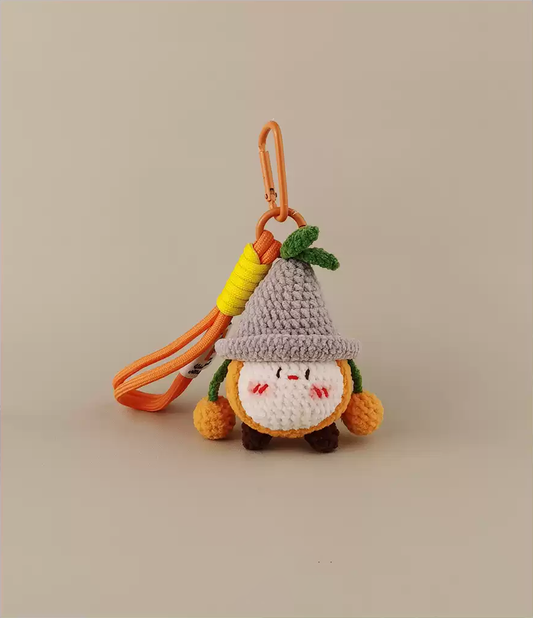 Cute, kawaii crochet little gnome keychain with an orange leather strap, a gray hat, and green leaves on it. A simple design against a white background.