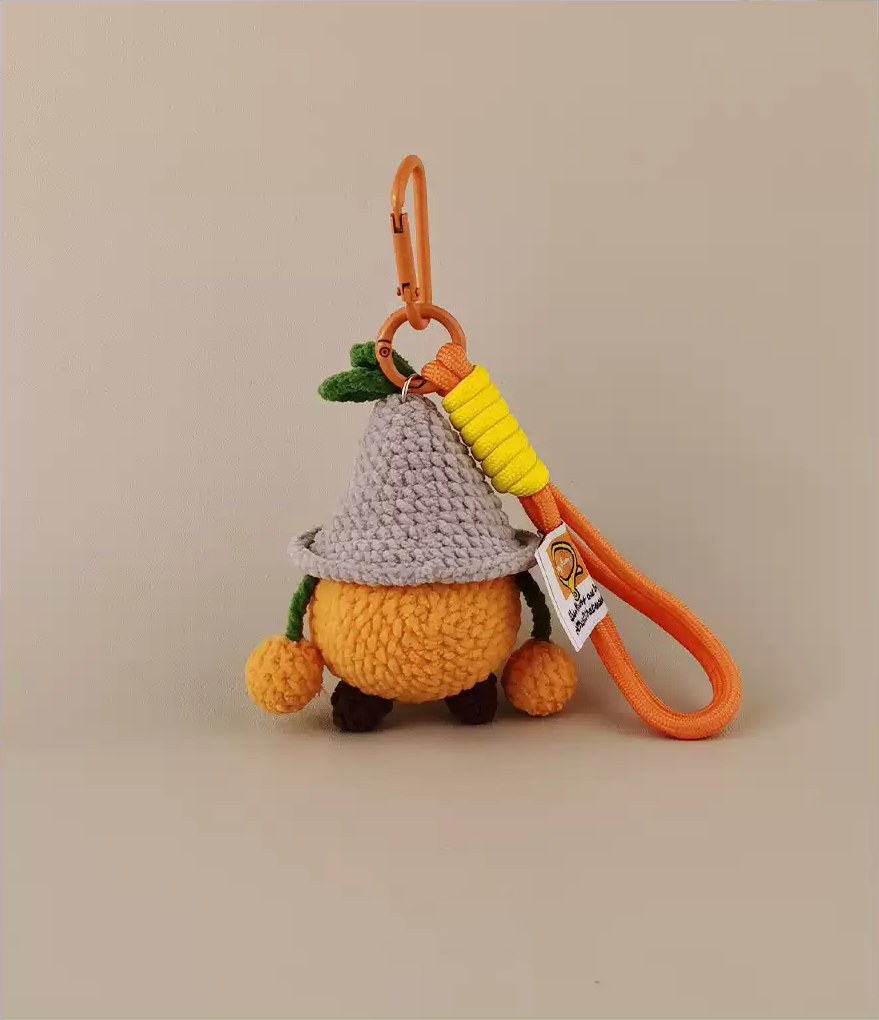 Cute amigurumi, a small orange character with a grey hat and yellow straw, as a keychain on a long plastic lanyard. 